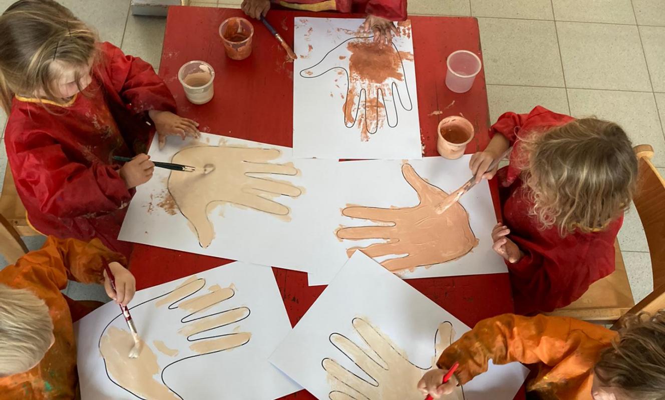 Foto van kleuters die tekeningen maken van handen in verschillende huidskleuren.